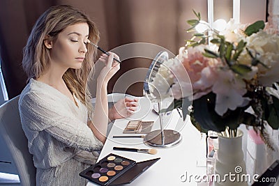 Amazing young woman doing her makeup in front of mirror. Portrait of beautiful girl near cosmetic table Stock Photo