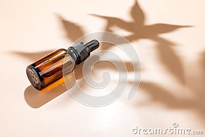Amber bottle with cannabis oil used for medical purposes on beige background with daylight and the shadow of a hemp leaf Stock Photo