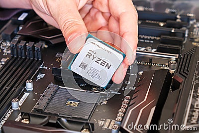 AMD Ryzen 3700X CPU in technician fingers, above a motherboard, part of a custom PC build Editorial Stock Photo