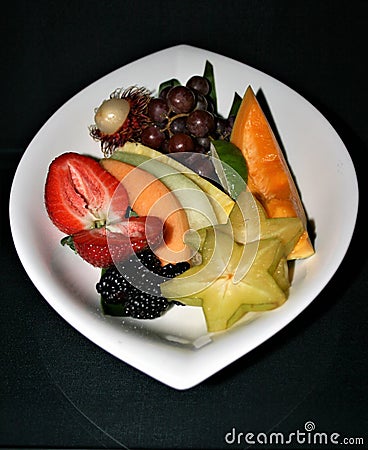 Closeup of a display of assorted sliced fruits on a white plate with a black background Stock Photo