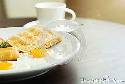 American breakfast and hot coffee in a white ceramic coffee cup on a wooden table with warm morning sunshine and lens flare Stock Photo