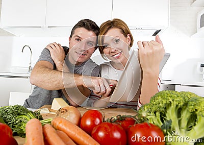 American couple in domestic kitchen wife following recipe in digital pad working together with husband Stock Photo
