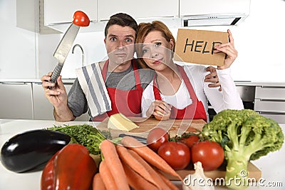 American couple in stress at home kitchen in cooking apron asking for help frustrated Stock Photo