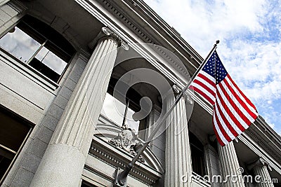 American Flag Blowing in the Wind in Front of Stone Column Building with blue sky and clouds Stock Photo