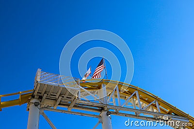 An American flag and a California flag on top of a yellow rollercoaster with a gorgeous blue sky at Santa Monica Pier Editorial Stock Photo