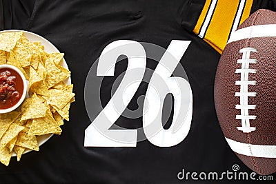 An American football with organic nacho chips and mild salsa on a white black football jersey with the 26 number on horizontal Stock Photo