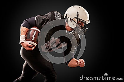 American football player in dark uniform with the ball is preparing to attack on a black background. Stock Photo