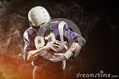 American football player holding ball in his hands in smoke. Black background, copy space. The concept of American Stock Photo