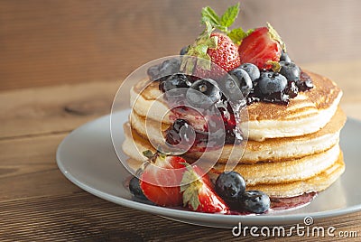 American pancakes or fritters served with strawberry and blueberry jam, delicious dessert for breakfast, rustic style, wooden back Stock Photo