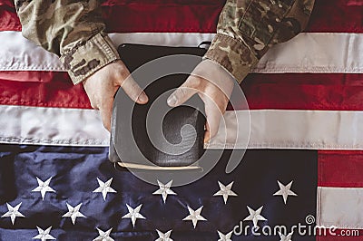 American soldier mourning and praying with the Bible in his hands and the American flag Stock Photo