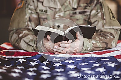 American soldier mourning and praying with the Bible in his hands and the American flag Stock Photo