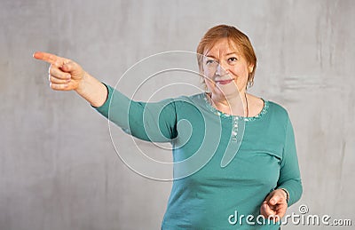 Amiable elderly woman in teal jumper pointing towards Stock Photo