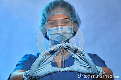 Ampoule with medicine, vaccine in hands of doctor in protective mask, gloves and uniform, closeup. Coronavirus disease COVID-19 Stock Photo