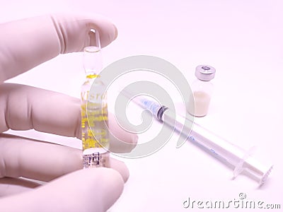 An ampule of medicine hold by hand with glove with a syringe and vaccine vial in background Stock Photo