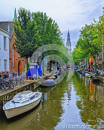 Amsterdam canal view with stationery boats, parked cycles and a monument in the distance Editorial Stock Photo
