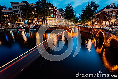 Amsterdam evening illuminated down town city. Touristic boat light trails and bridge reflections at the Leidsegracht and Stock Photo