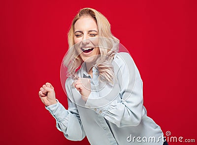 Amused beautiful young woman with closed eyes and clenched fists, isolated on red background. Yes concept. Amusing girl celebrates Stock Photo