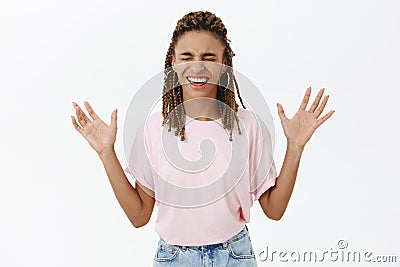 Amused and joyful carefree African-American woman with dreads in pink t-shirt closing eyes raising arms with palms faces Stock Photo