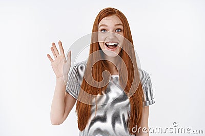 Amused outgoing lively redhead cute girl blue eyes widen eyes happily waving raised palm hello hi welcome gesture Stock Photo