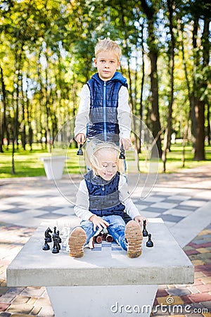 Amusing boy and girl playing chess together in park. Chess club for kids. Happy childhood and kids friendship. Logic game for Stock Photo