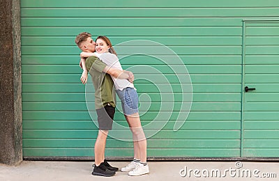 Amusing couple lovers hugging and kissing the background of a green wall on the street. Funny couple in love with a turquoise Stock Photo