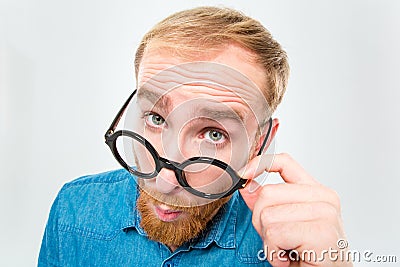 Amusing young man with beard looking over black round glasses Stock Photo