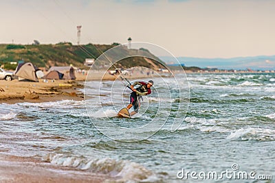 Anapa, Russia - July 9, 2017: Man kitesurfer rides kite through splashing waves by sandy shore of Black Sea. Popular kitesurf Editorial Stock Photo