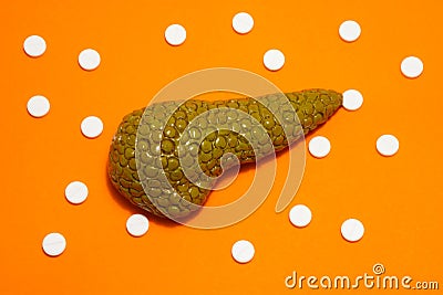 Anatomical realistic figure or model of human or animal pancreas gland on orange background, surrounded by white tablets or pills, Stock Photo