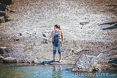 Anchorage Alaska USA - Woman in rubber boots and fishing vest fishes for salmon in Ship Creek near downtow Editorial Stock Photo