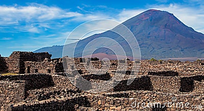 ancient archeology of stone houses with a volcano in the background Stock Photo