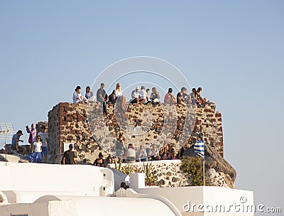 Santorini, Greece - June 05 2012: Tourists sit on an old ruined wall waiting for the sunse Editorial Stock Photo