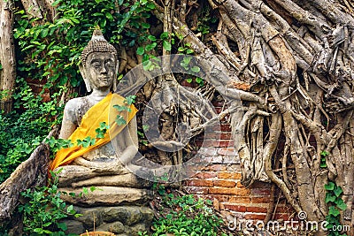 Ancient Buddha Statue with tree roots and brick wall background Editorial Stock Photo