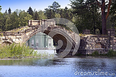 The ancient destroyed bridge in park and pavilion of Venus (1793) is visible under a bridge arch. Gatchina, St. Petersburg, Russia Stock Photo