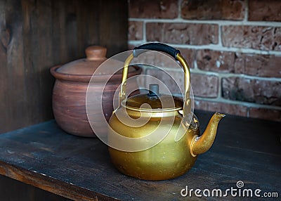 Ancient gold kettle on old wooden shelf. Classic teapots to use for drinking tea or coffee. Clay pot in the background Stock Photo