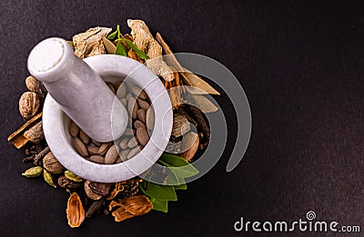 Ancient medicine systems concept. Top view of ayurvedic tablets in a mortar and different spices, green leaves on black background Stock Photo