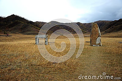 An ancient menhir and a ritual stone arch of soyat in the center of the autumn steppe surrounded by mountains Stock Photo