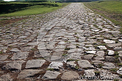 Ancient road paved with cobblestone and going up through hills. Stock Photo