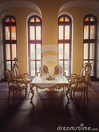 Ancient royalty dining room, medieval furniture style with golden ornate chairs and table near the arched windows. Luxury hosting Stock Photo