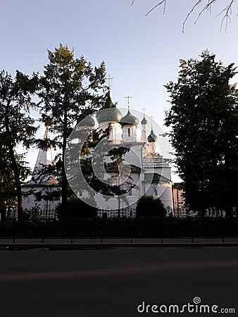 White Orthodox Church, hidden behind dark fir trees in the rays of the setting sun. Stock Photo