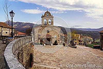 Ancient stone church in medieval village with old houses and blue sky with clouds. La Hiruela Madrid Stock Photo