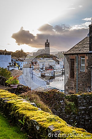 Ancient stone wall covered with moss diagonally in the foreground with a stone house on the left and the Tarbert Free Church Editorial Stock Photo