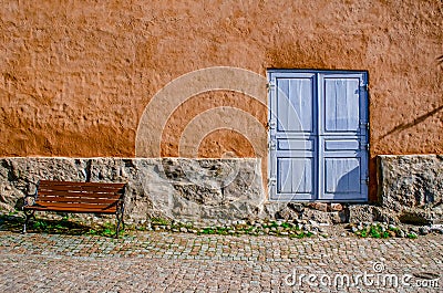 An ancient textured wall with a stone basement, a blue door and a bench. Stock Photo