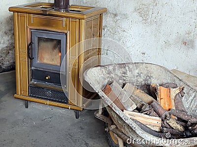 Tiled stove and wheelbarrow full of firewood in the old mountain Stock Photo