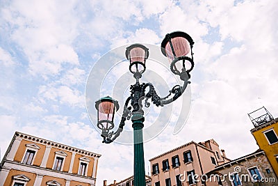 An ancient triple metal street lamp, with pink plafonds against the sky and buildings of Venice, Italy. Vintage street Stock Photo