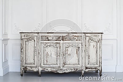 Ancient white commode bureau with paint peeled off on luxury wall design bas-relief stucco mouldings roccoco elements Stock Photo