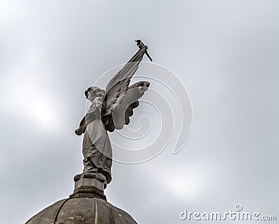 Angel sculpture and a magpie against the cloudy sky Editorial Stock Photo