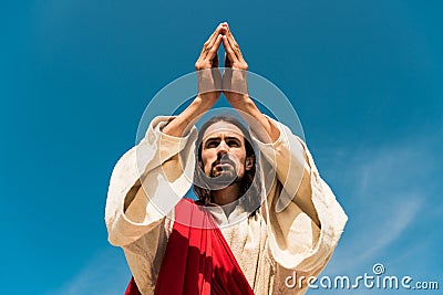 Angle view of jesus with praying hands against blue sky Stock Photo