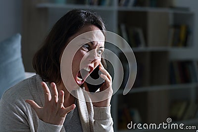 Angry adult woman screaming calling on phone at night at home Stock Photo