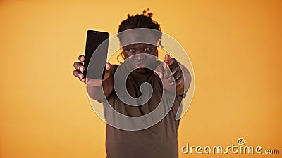 Angry african american black man showing phone screen and pointing finger towards camera. Cheated husband accusing his Stock Photo