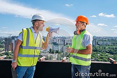 Angry boss yelling in megaphone at his builder on construction site Stock Photo